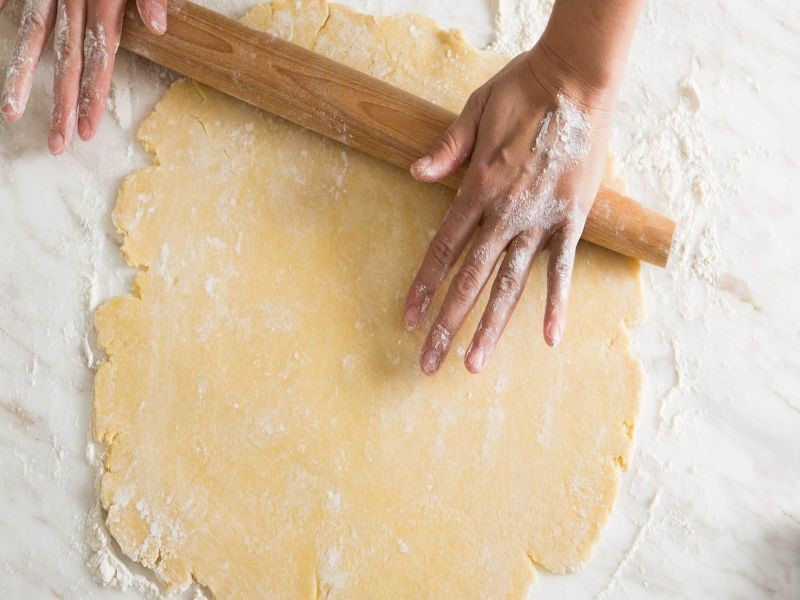 Hands holding a rolling pin rolling out dough