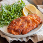 Photo of a plate of chicken schnitzel, arugula and lemon wedges