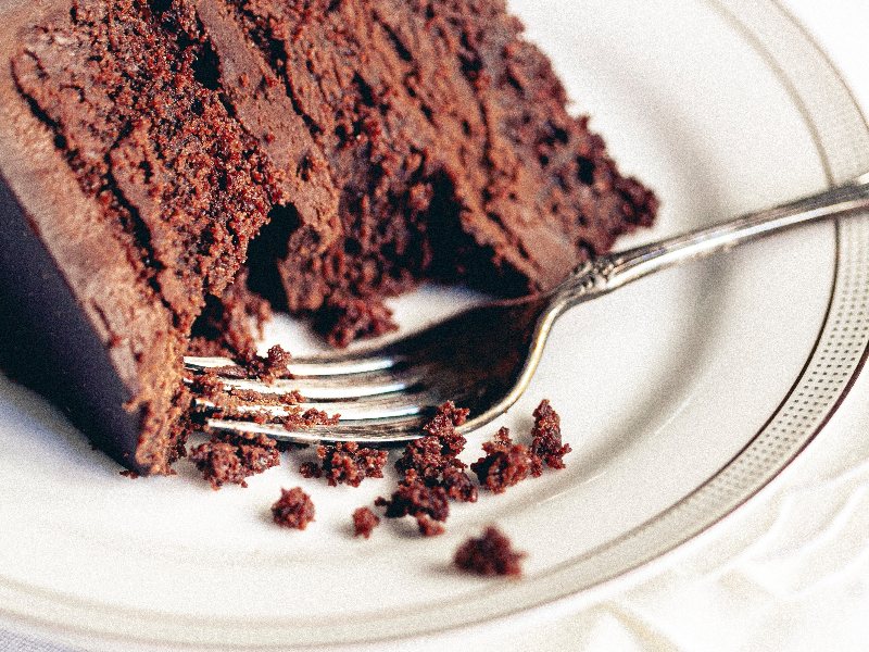 A photo of a piece of chocolate layer cake on a plate with a fork