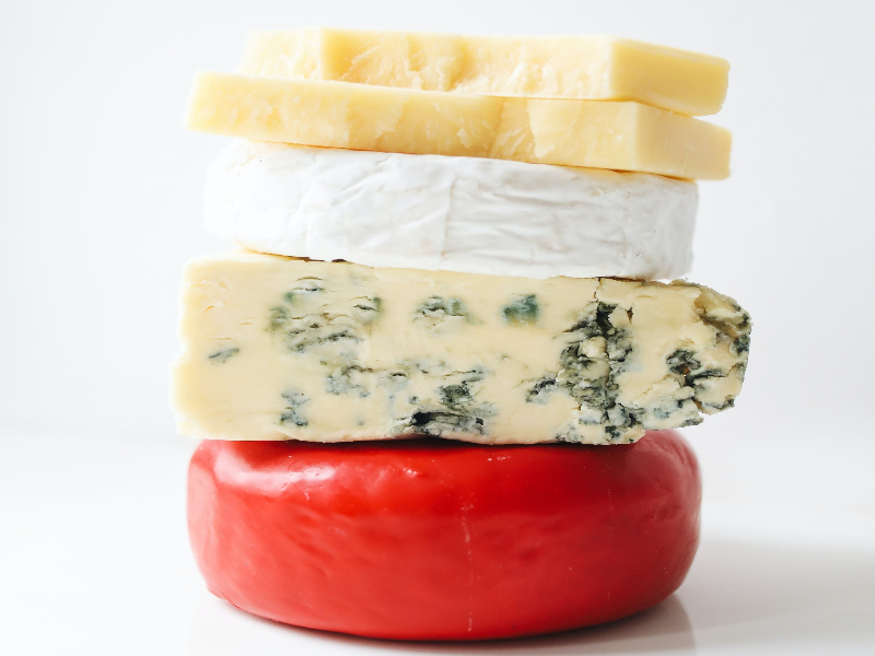 A photo of 4 cheese stacked on top of each other: gouda, blue, brie and parmesan.