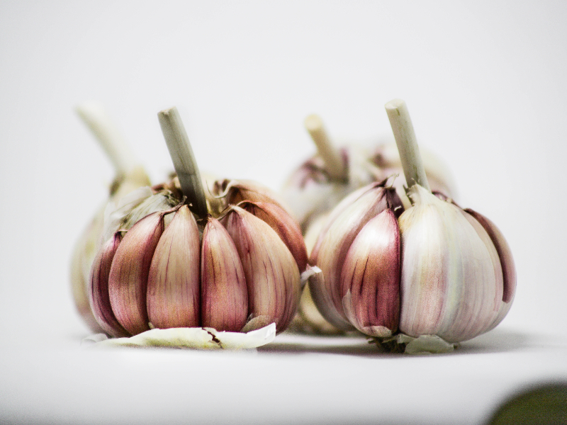 A photo of two garlic bulbs with some of the outer skin removed to show reddish cloves.