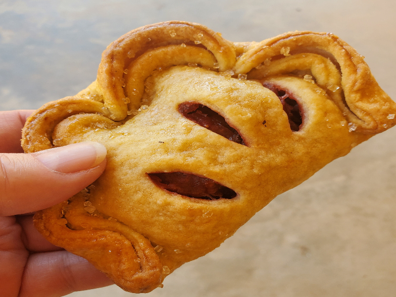 Photograph of a hand holding a mixed berry hand pie.