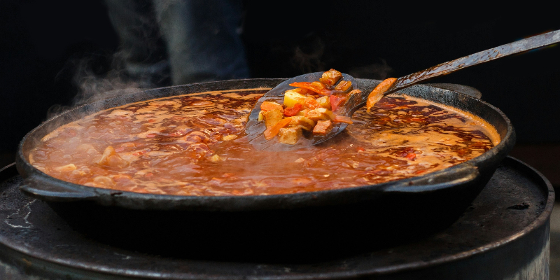 Photo of a large cast iron skillet with food cooking and steam rising from pan.