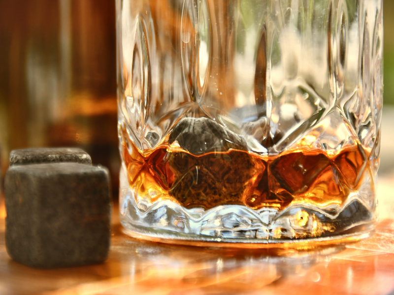 Photo of whiskey in a cut crystal glass with a few whiskey rocks in the glass and a few nest to the glass.