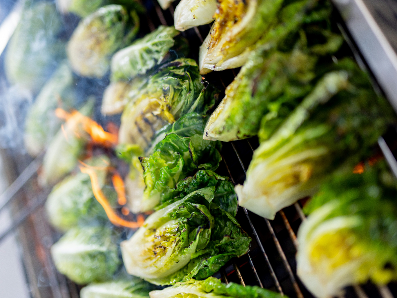 Romaine lettuce on a gas grill with flames as it chars.
